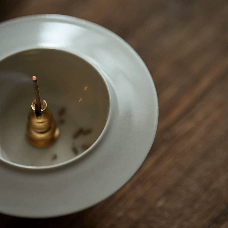 Small incense burner with a lit stick on a wooden surface