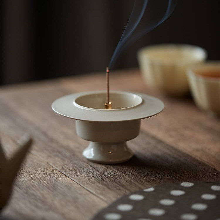 Incense stick burning in a white ceramic holder on a wooden surface with a dark background