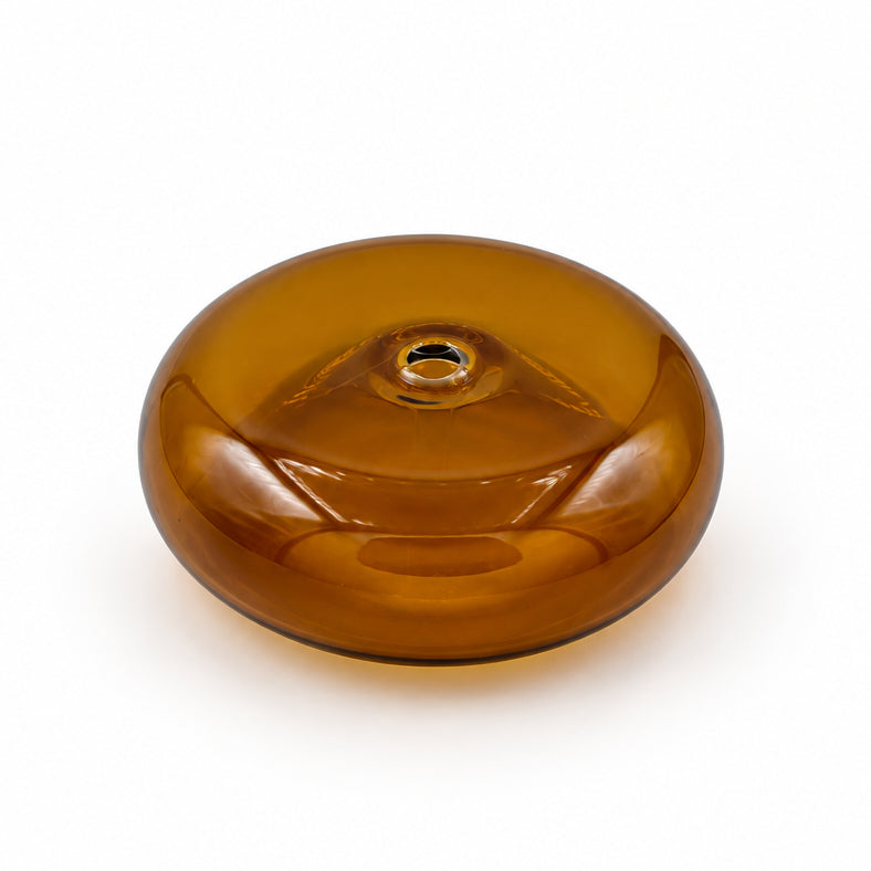 A single round amber-brown glass bead with a geometric cutout design, resting on a white and gray veined marble surface.