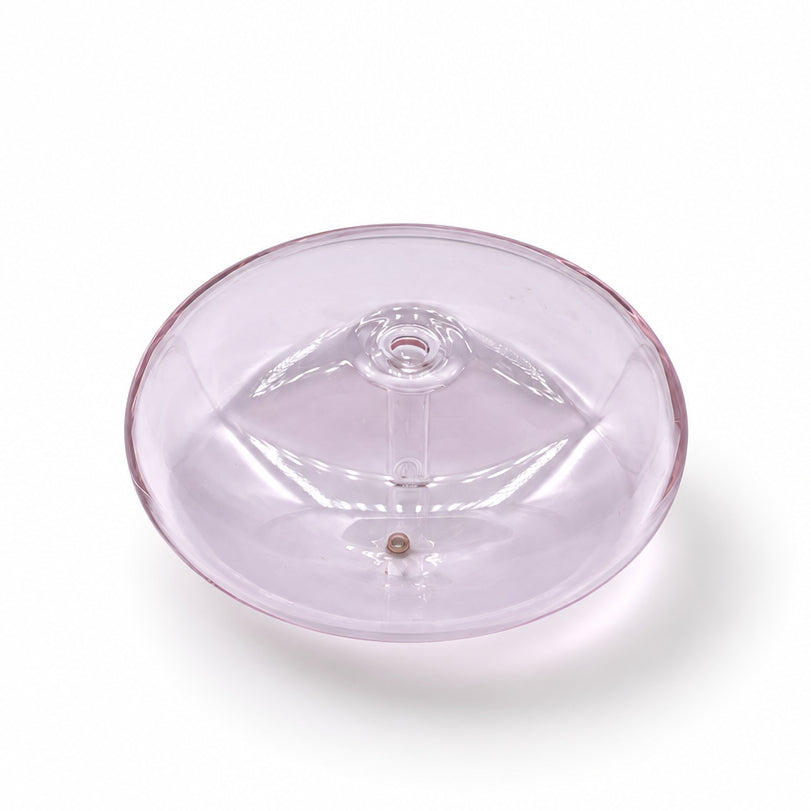 A small round translucent lavender glass dish or candle base with a decorative embossed design, placed on a white marble surface with gray veining.