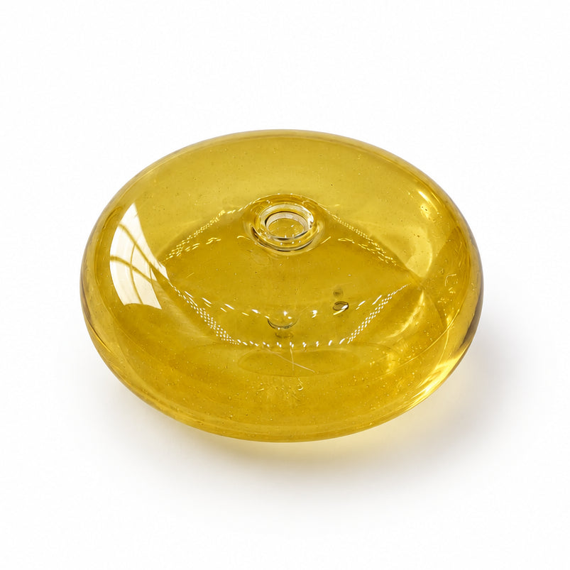 A small, round, translucent yellow glass dish or candle holder with a textured pattern inside, resting on a white and gray marble surface.