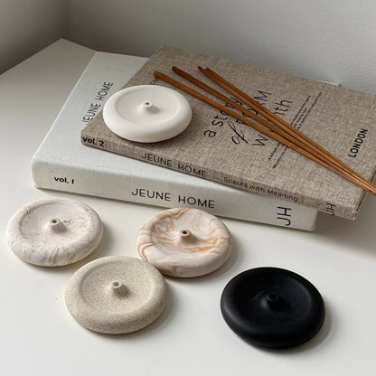 Four round ceramic coasters in white, beige, and black, styled on a white surface with a linen book and wooden chopsticks.