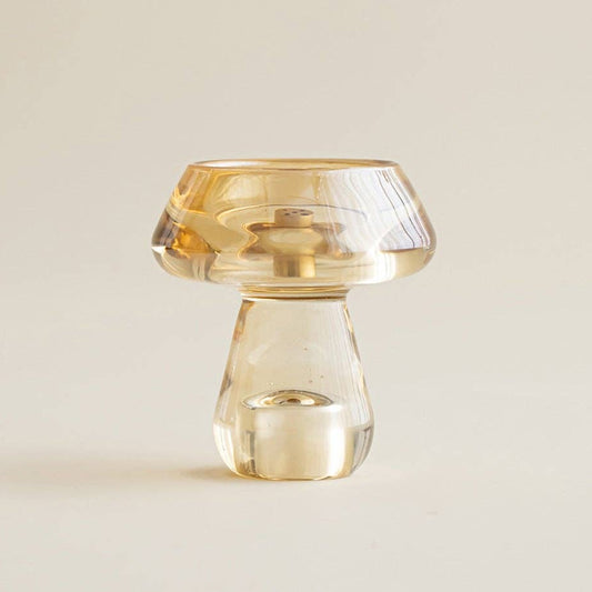 A small mushroom-shaped clear glass candle holder with a frosted amber-colored top, shown on a warm off-white background. The brand name 'Gohúbi London' is visible in the bottom right corner.