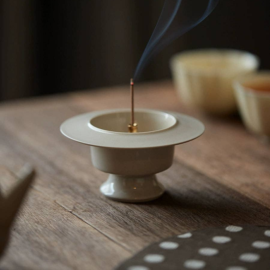Incense stick burning in a white ceramic holder on a wooden surface with a blurred background