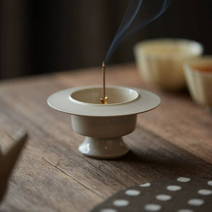 Incense stick burning in a white ceramic holder on a wooden surface with a blurred background