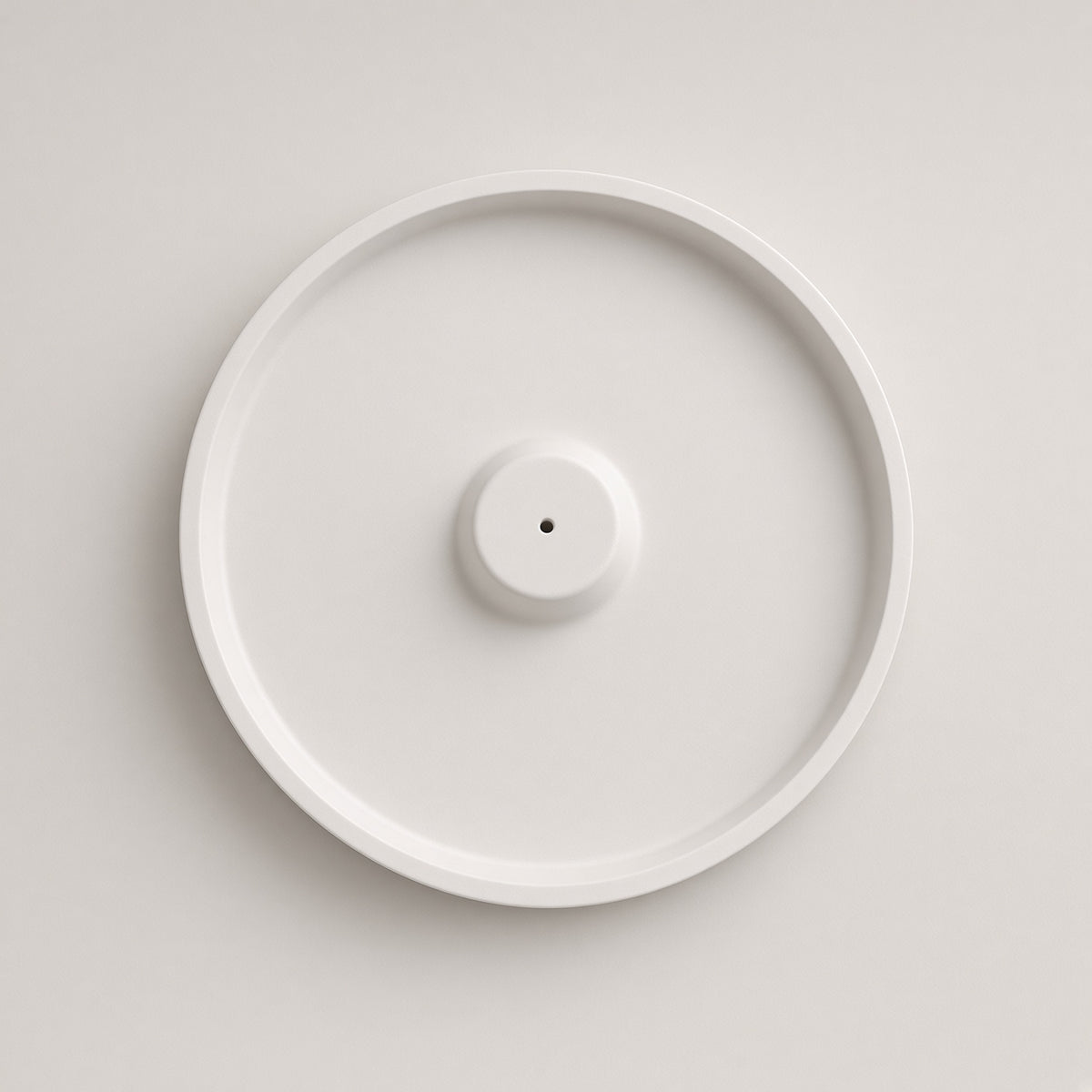 A minimalist white circular wall-mounted light fixture or decorative plate with a central dome and small hole, shown against a matching light gray wall.